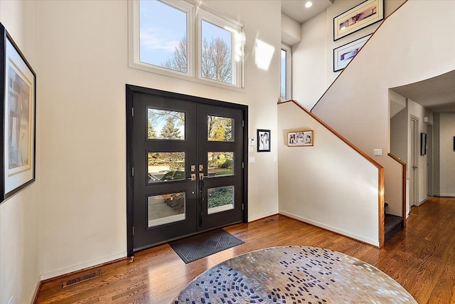 foyer entrance featuring wood finished floors, a towering ceiling, stairs, baseboards, and french doors