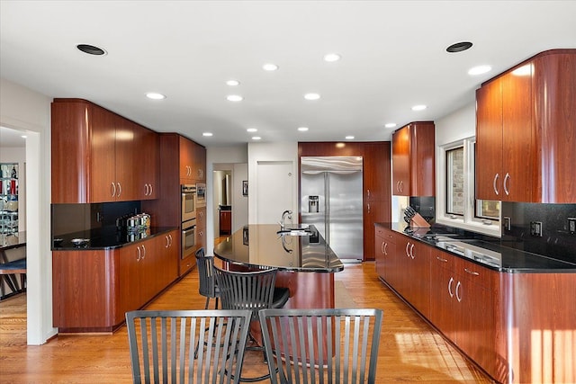 kitchen featuring stainless steel appliances, light wood-style flooring, an island with sink, a sink, and recessed lighting