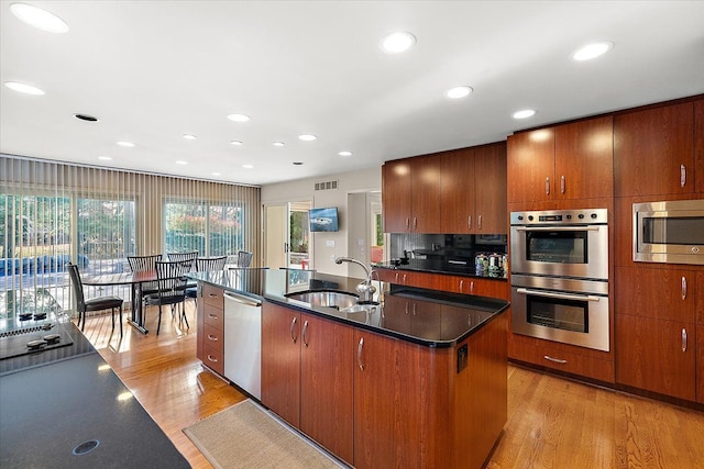 kitchen featuring stainless steel appliances, a sink, dark countertops, light wood-type flooring, and recessed lighting