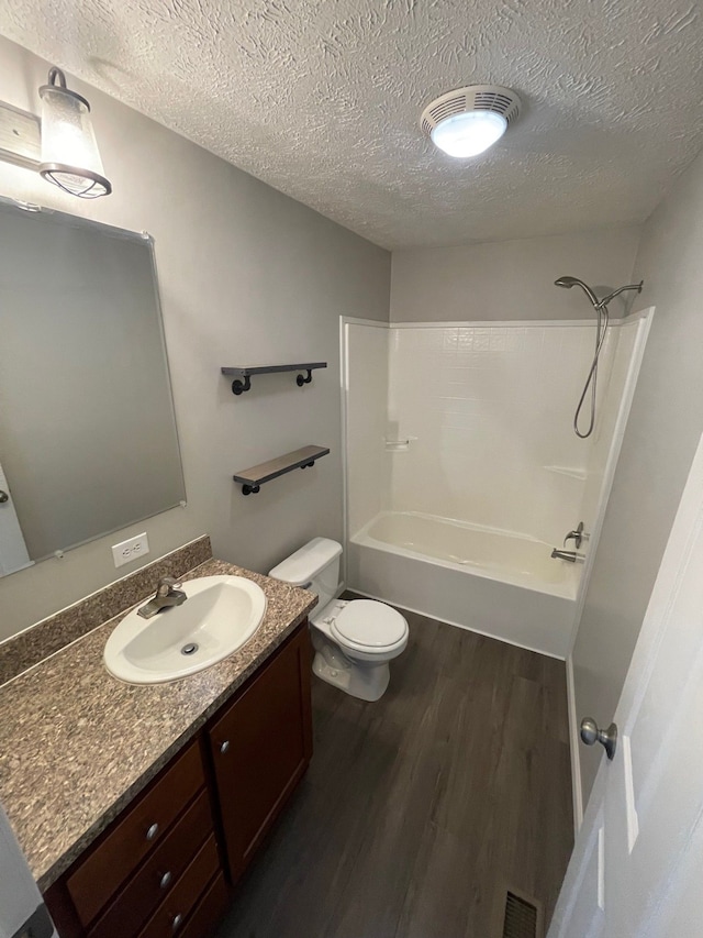 full bathroom with wood finished floors, a textured ceiling, toilet, washtub / shower combination, and vanity