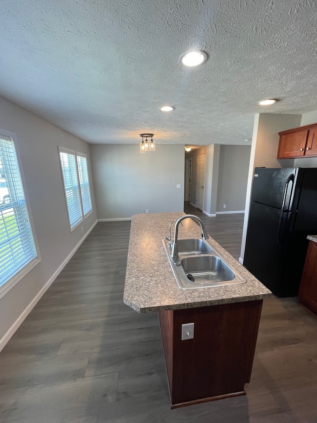 kitchen with freestanding refrigerator, a sink, baseboards, a textured ceiling, and an island with sink