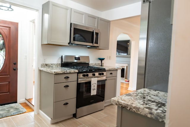 13185 Sycamore St, Southgate, MI 48195 - kitchen featuring appliances with stainless steel finishes, gray cabinets, light wood-style floors, arched walkways, and light stone countertops