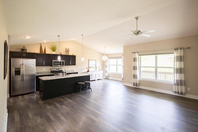 kitchen featuring stainless steel appliances, dark wood-type flooring, a ceiling fan, a kitchen island with sink, and a breakfast bar