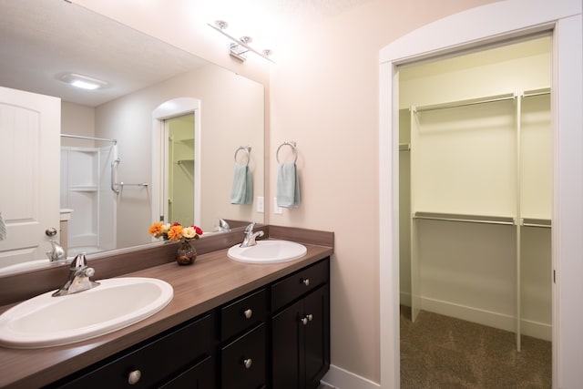 full bathroom featuring double vanity, a shower, and a walk in closet