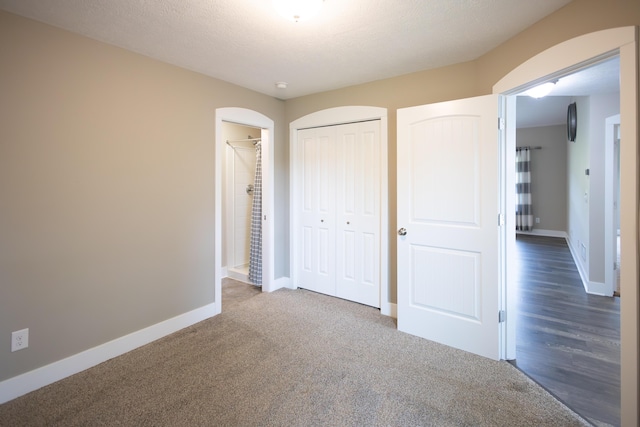 unfurnished bedroom with arched walkways, baseboards, carpet, and a closet