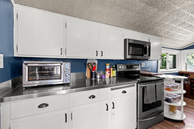 638 E Michigan Ave, Grass Lake, MI 49240 - kitchen with stainless steel counters, stainless steel appliances, white cabinetry, wood finished floors, and an ornate ceiling