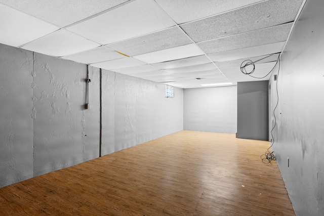 below grade area with a paneled ceiling and wood finished floors