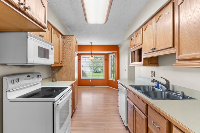kitchen featuring white appliances, a sink, light wood-type flooring, light countertops, and a textured ceiling