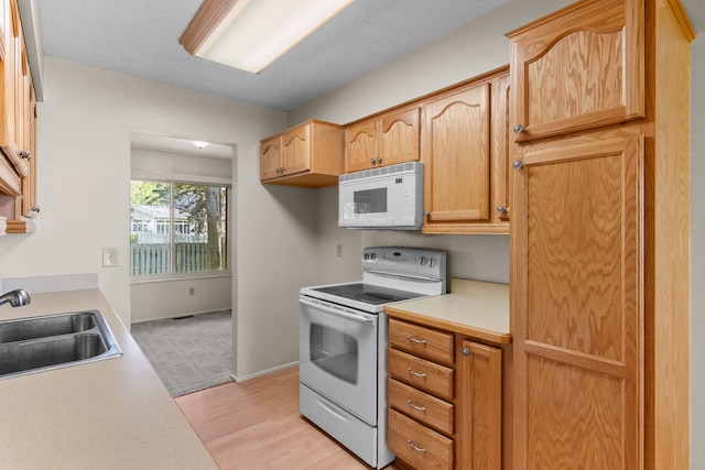 kitchen with white appliances, a sink, light countertops, and baseboards