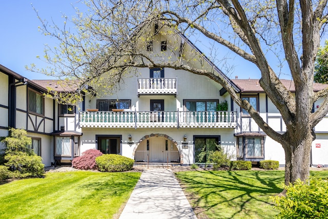 view of front facade featuring stucco siding, a balcony, and a front yard