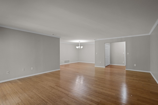 empty room with a chandelier, light wood-style flooring, ornamental molding, and baseboards