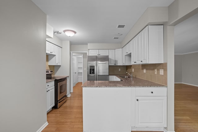 kitchen with stainless steel appliances, a sink, a peninsula, light wood-style flooring, and tasteful backsplash