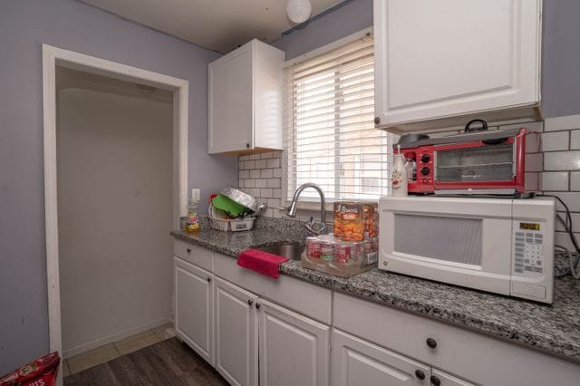 kitchen with white microwave, a sink, white cabinets, and light stone counters