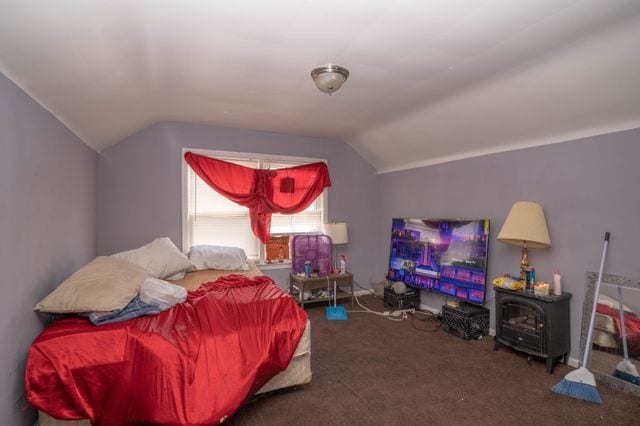 carpeted bedroom featuring vaulted ceiling and a wood stove