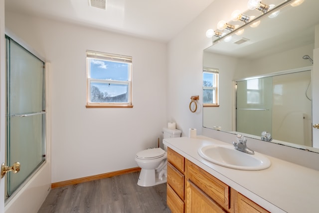bathroom with wood finished floors, toilet, vanity, baseboards, and enclosed tub / shower combo