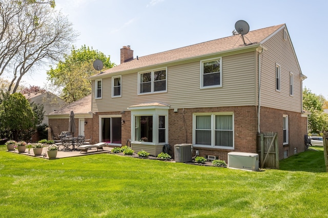 back of property with a chimney, cooling unit, brick siding, a patio area, and a lawn