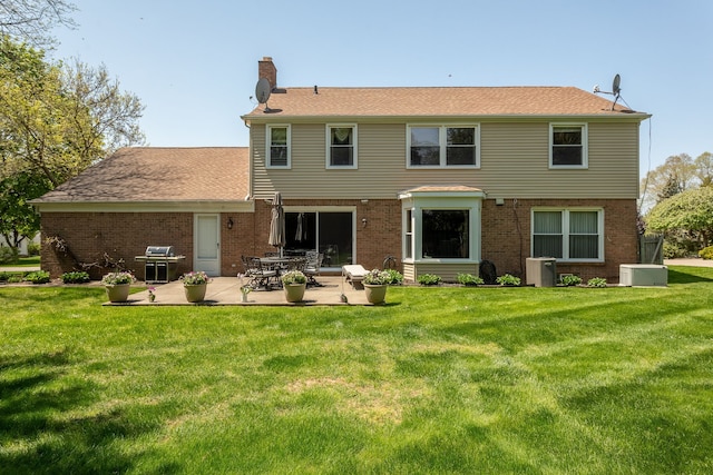 rear view of house with a chimney, a patio, a yard, and brick siding