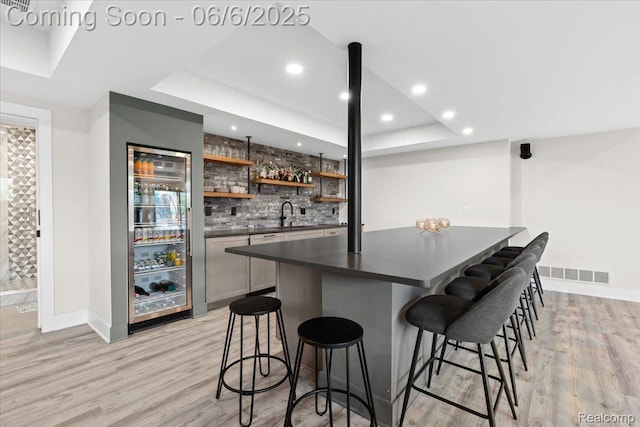 10611 Stoney Point Dr, South Lyon, MI 48178 - indoor wet bar with tasteful backsplash, light wood-style flooring, a tray ceiling, baseboards, and recessed lighting