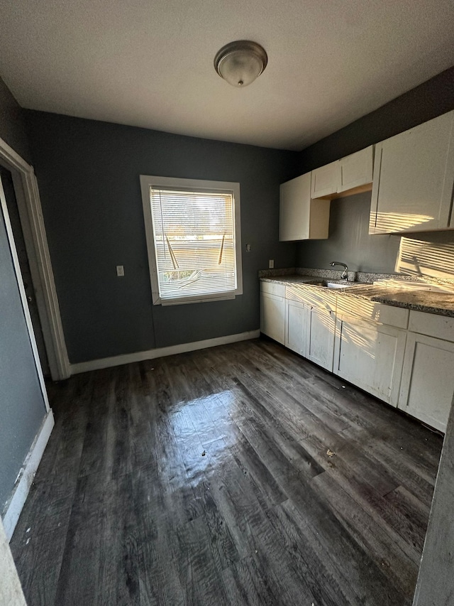 kitchen with white cabinets, a sink, dark wood-style floors, and baseboards