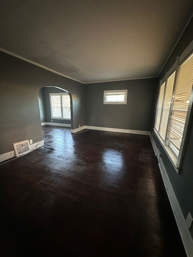 empty room featuring arched walkways, baseboards, dark wood-style floors, plenty of natural light, and crown molding