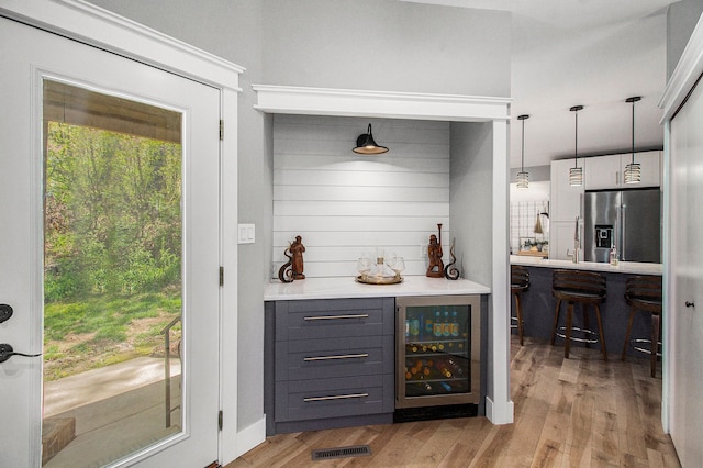 8440 Lance, Brighton, MI 48116 - indoor dry bar featuring wine cooler, stainless steel refrigerator with ice dispenser, light wood-style floors, and decorative light fixtures