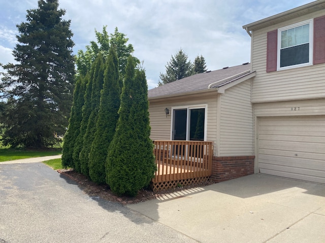 view of home's exterior featuring driveway, a garage, a wooden deck, and brick siding