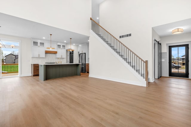 unfurnished living room with light wood finished floors, a towering ceiling, a barn door, recessed lighting, and baseboards