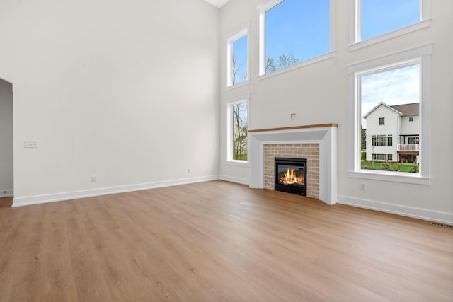 unfurnished living room featuring a towering ceiling, light wood-style floors, a brick fireplace, and baseboards