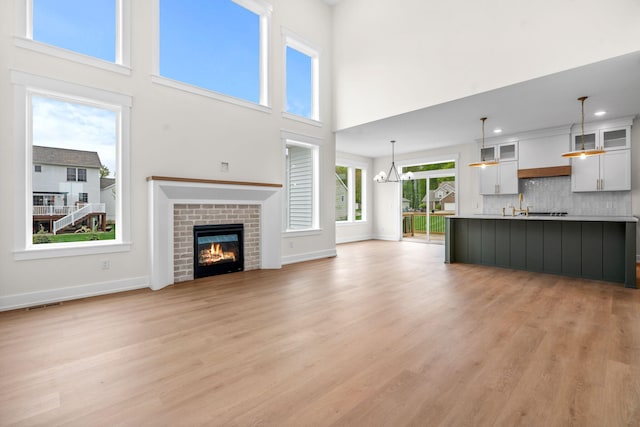 unfurnished living room featuring light wood-style floors, a brick fireplace, a chandelier, baseboards, and recessed lighting