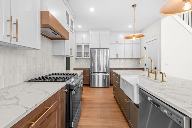 kitchen with appliances with stainless steel finishes, premium range hood, a sink, white cabinetry, and glass insert cabinets