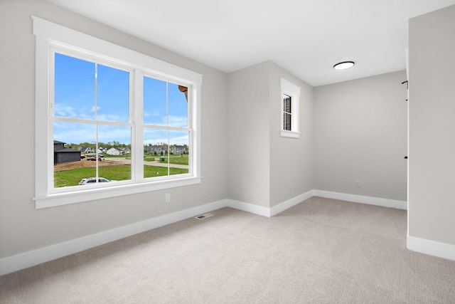 spare room featuring light colored carpet and baseboards