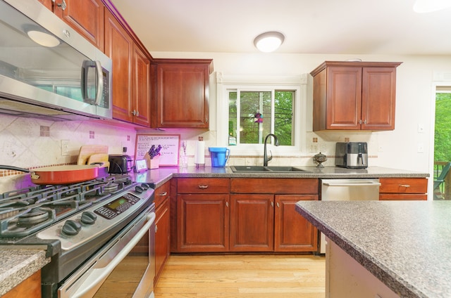 1418 Trailside Blvd, Wixom, MI 48393 - kitchen featuring appliances with stainless steel finishes, a sink, light wood finished floors, backsplash, and dark countertops