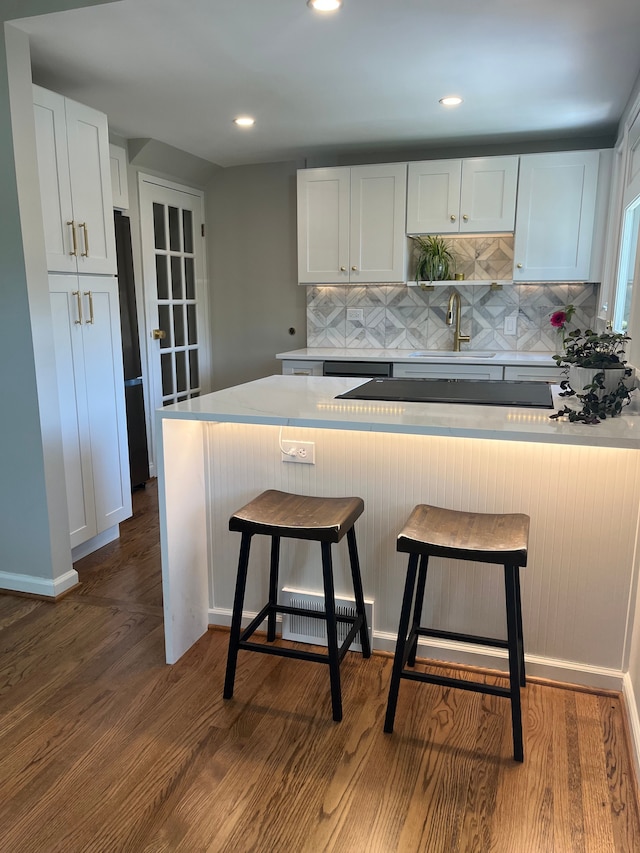 kitchen with a sink, backsplash, a kitchen bar, white cabinetry, and recessed lighting