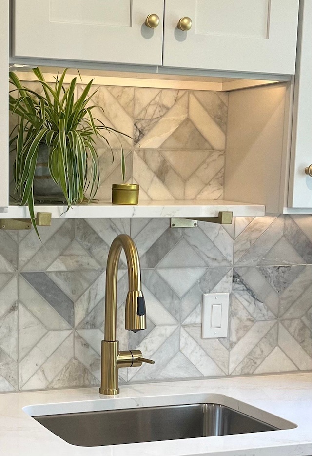 detailed view of a sink, light stone countertops, and tasteful backsplash