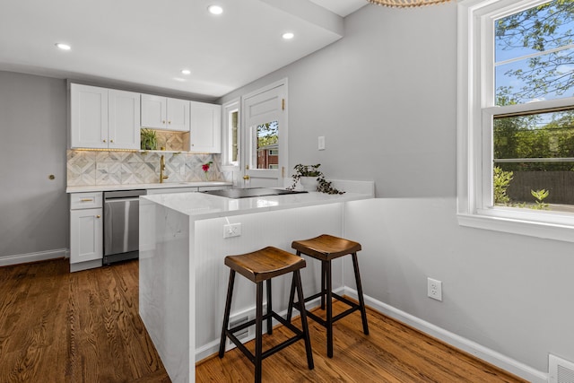 kitchen featuring stainless steel dishwasher, cooktop, recessed lighting, dark wood finished floors, and a breakfast bar