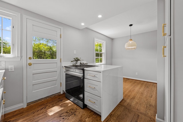 kitchen featuring a peninsula, stainless steel electric range, dark wood-style flooring, light countertops, and baseboards