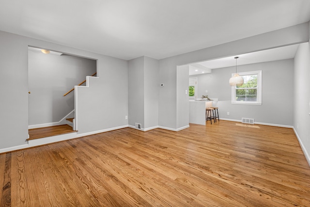unfurnished living room featuring light wood finished floors, stairway, and baseboards