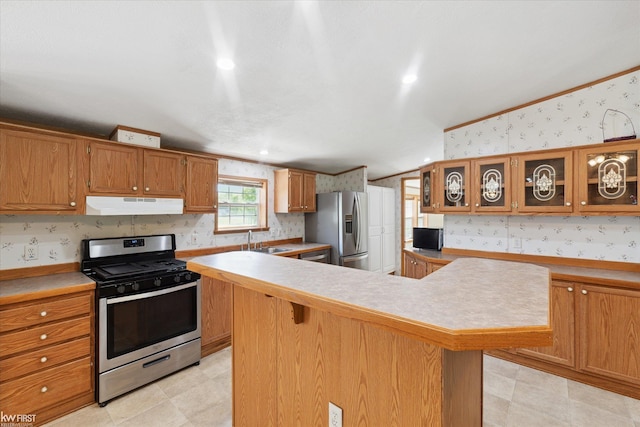 kitchen featuring appliances with stainless steel finishes, wallpapered walls, under cabinet range hood, a sink, and light countertops