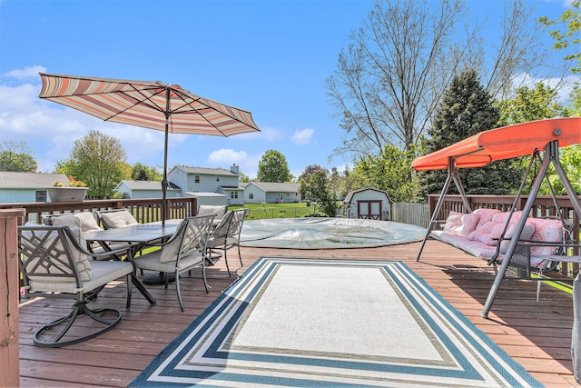 wooden terrace featuring outdoor dining space, a storage shed, an outdoor structure, and a residential view