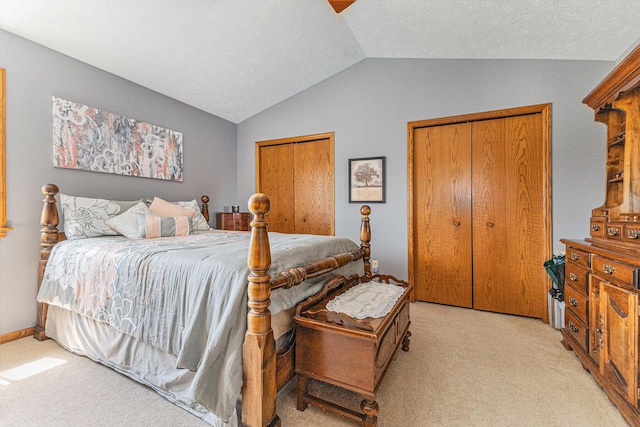 bedroom featuring vaulted ceiling, light carpet, and multiple closets