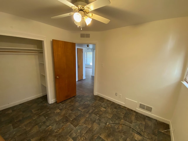 unfurnished bedroom with baseboards, dark stone finish floors, a closet, and a ceiling fan