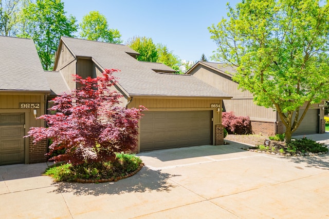 mid-century inspired home with driveway, a garage, a shingled roof, and brick siding