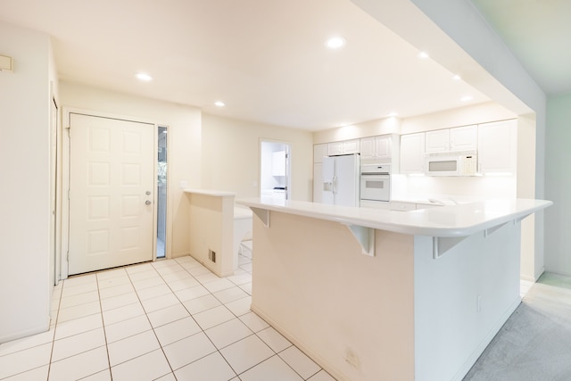 kitchen with white appliances, a breakfast bar, recessed lighting, light countertops, and white cabinetry