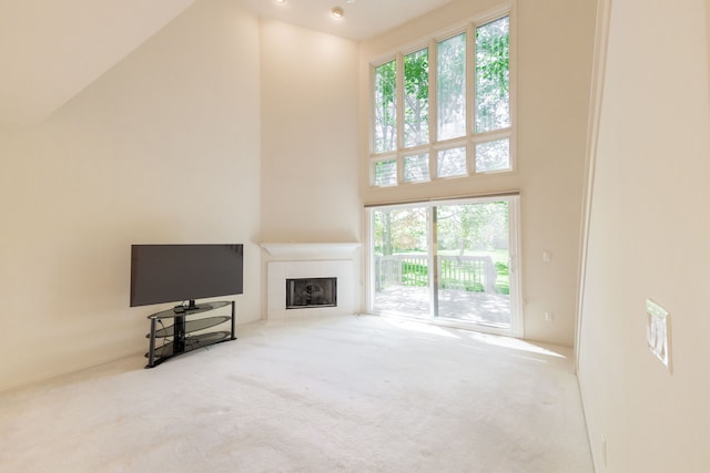 unfurnished living room featuring a high ceiling, carpet flooring, a fireplace, and plenty of natural light