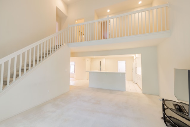 unfurnished living room with a high ceiling, recessed lighting, light carpet, and stairs