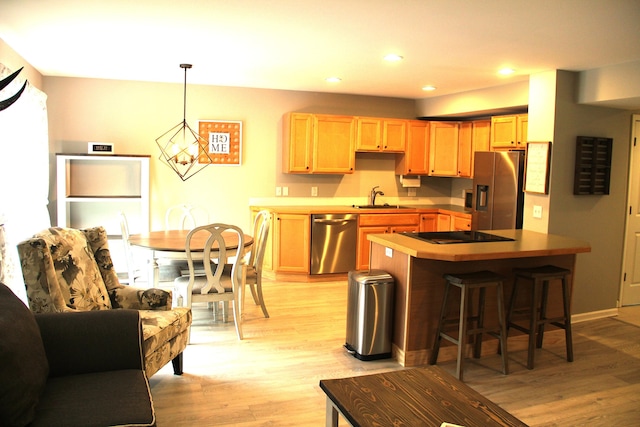 kitchen featuring appliances with stainless steel finishes, a sink, light wood finished floors, a breakfast bar, and light brown cabinets