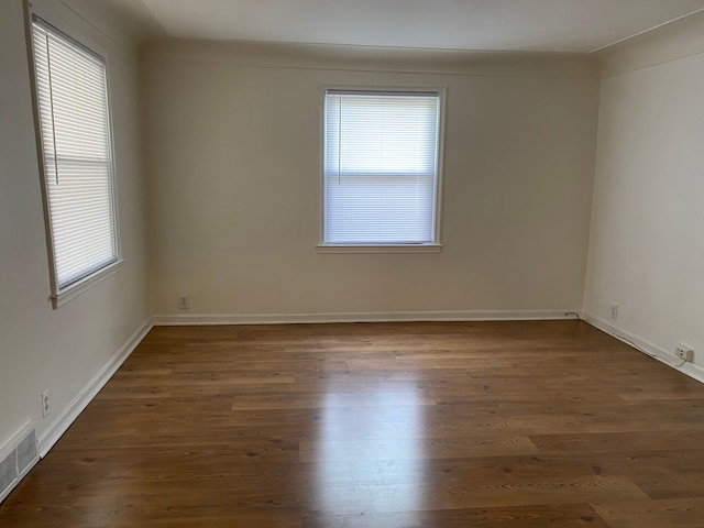 unfurnished room featuring healthy amount of natural light, dark wood finished floors, and baseboards