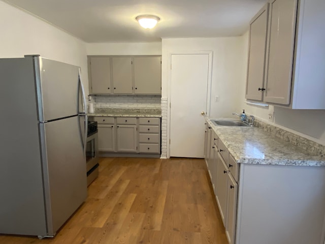 kitchen featuring stainless steel appliances, a sink, light wood-type flooring, gray cabinets, and decorative backsplash