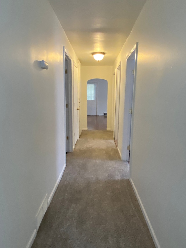 hallway featuring arched walkways, carpet flooring, and baseboards