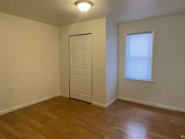 unfurnished bedroom featuring wood finished floors, baseboards, and a closet